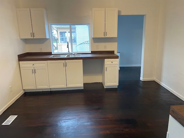 kitchen with white cabinetry, sink, built in desk, and dark wood-type flooring