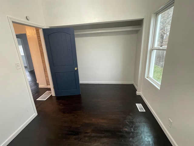 unfurnished bedroom with multiple windows, a closet, and dark wood-type flooring