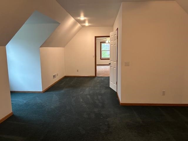 additional living space featuring dark carpet and vaulted ceiling