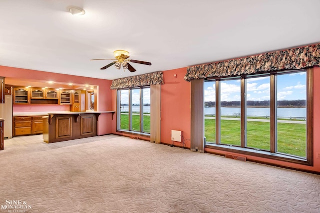 unfurnished living room featuring ceiling fan, a water view, and light colored carpet