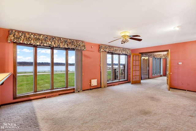 unfurnished room with light carpet, a water view, and ceiling fan