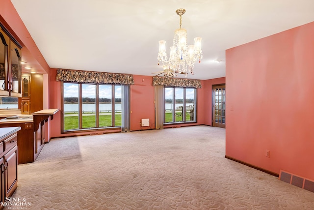 unfurnished living room featuring light carpet, a water view, and an inviting chandelier