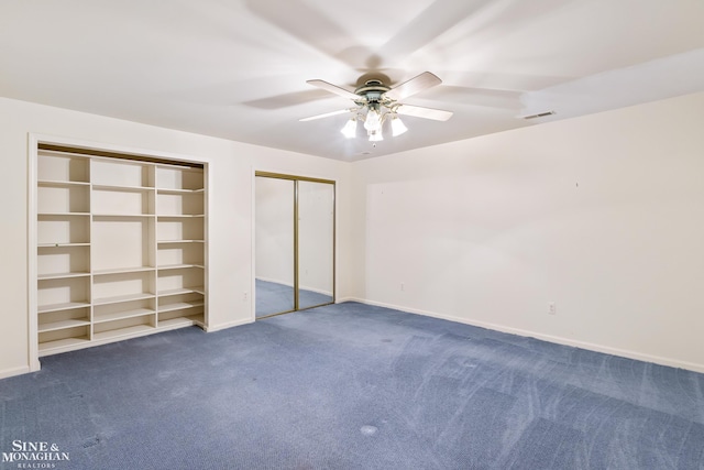 unfurnished bedroom with dark colored carpet, ceiling fan, and two closets