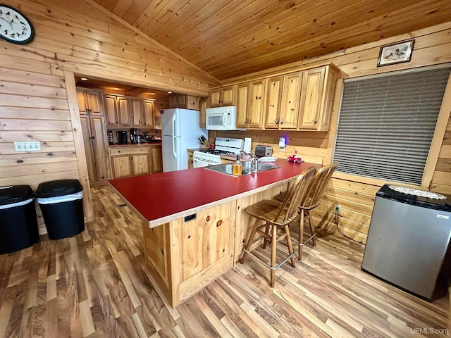 kitchen featuring a breakfast bar, white appliances, sink, vaulted ceiling, and light wood-type flooring