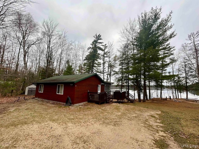 view of property exterior with a deck with water view and a storage unit