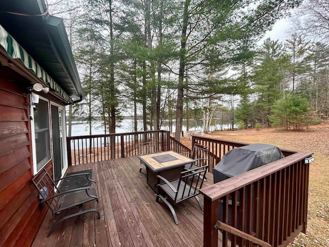 wooden deck with area for grilling, a water view, and an outdoor fire pit