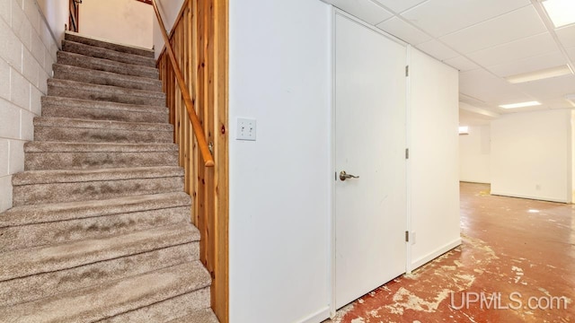 stairs with a paneled ceiling and concrete flooring