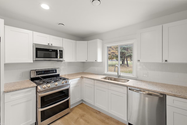 kitchen with white cabinets, sink, appliances with stainless steel finishes, light hardwood / wood-style floors, and light stone counters