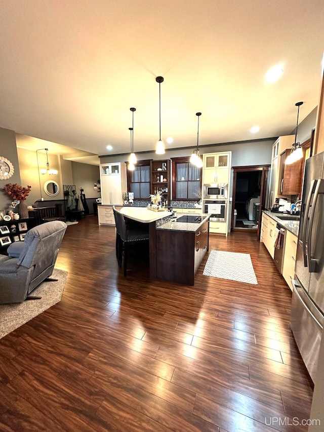 kitchen featuring appliances with stainless steel finishes, decorative light fixtures, dark wood-type flooring, and an island with sink