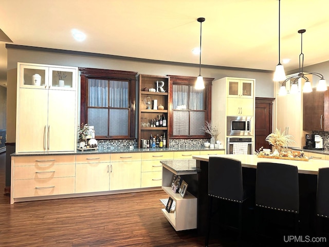 kitchen featuring backsplash, stainless steel appliances, pendant lighting, cream cabinetry, and dark hardwood / wood-style floors