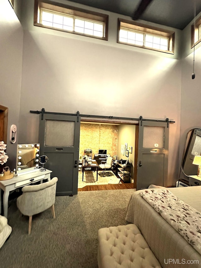 carpeted bedroom featuring a barn door, a high ceiling, and multiple windows