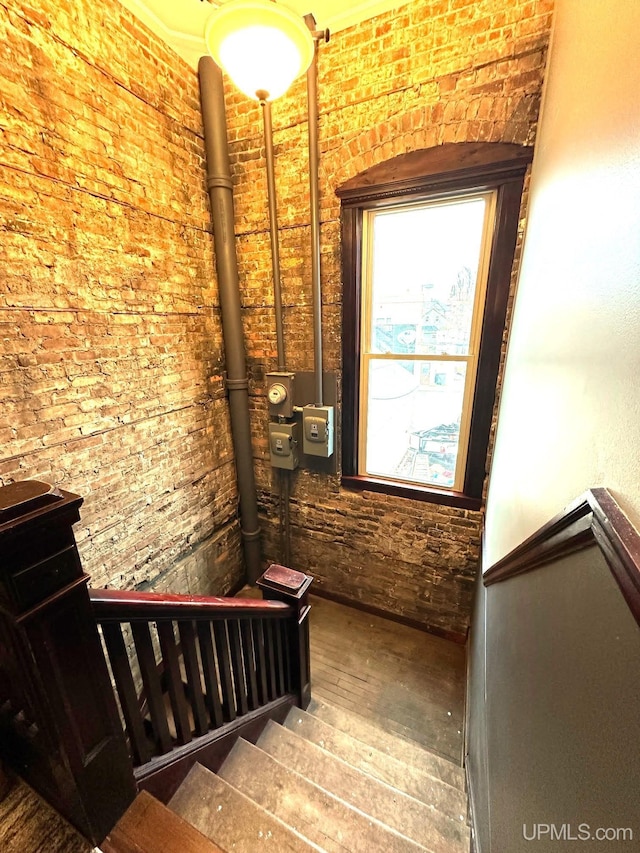 stairway with hardwood / wood-style floors and brick wall