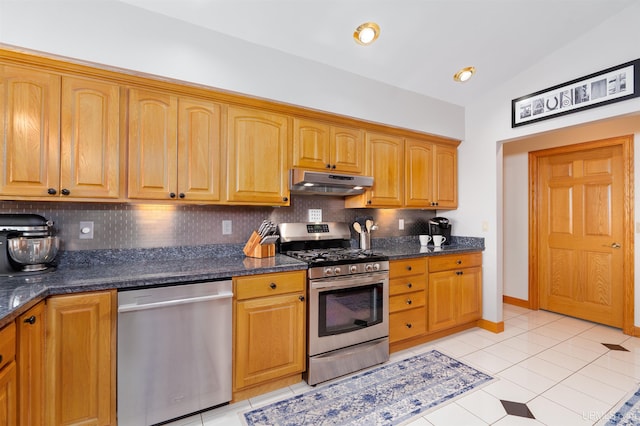 kitchen with tasteful backsplash, dark stone counters, stainless steel appliances, vaulted ceiling, and light tile patterned flooring