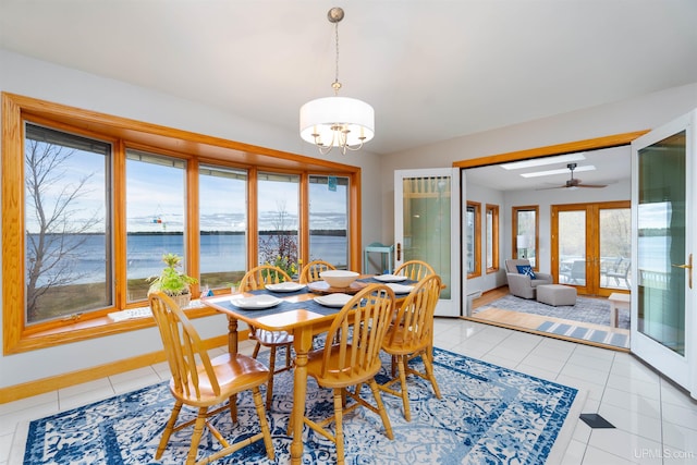 dining space with ceiling fan with notable chandelier, a water view, light tile patterned floors, and french doors