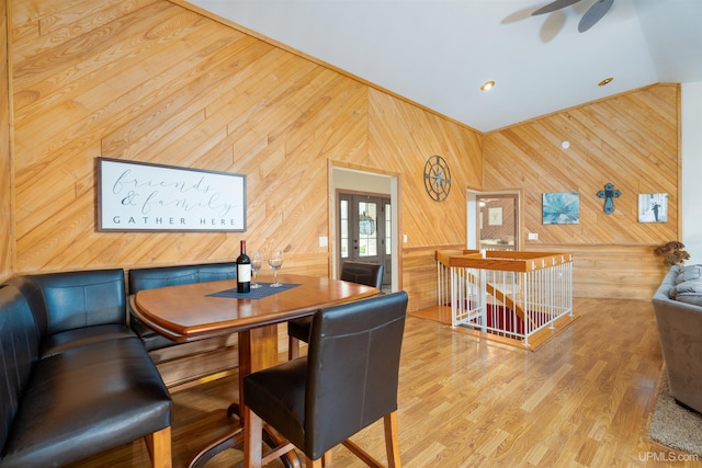 dining room with wood walls, light hardwood / wood-style flooring, ceiling fan, and vaulted ceiling