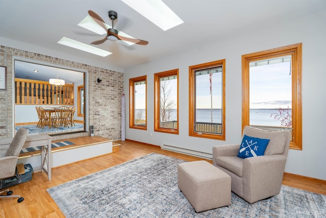 living area with hardwood / wood-style floors, a baseboard radiator, ceiling fan, and brick wall