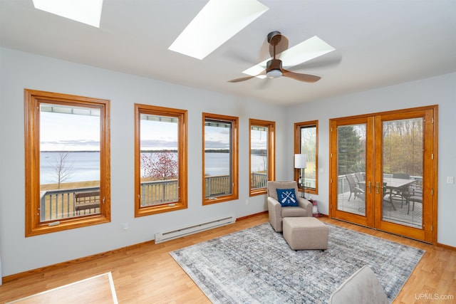 sitting room with a skylight, plenty of natural light, a baseboard radiator, and light wood-type flooring