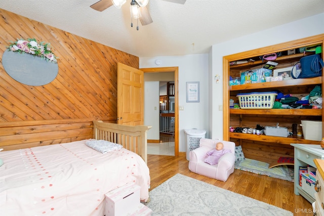 bedroom featuring a textured ceiling, light hardwood / wood-style floors, ceiling fan, and wood walls