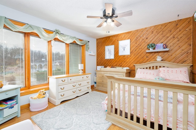 bedroom with a textured ceiling, light hardwood / wood-style floors, ceiling fan, and wood walls