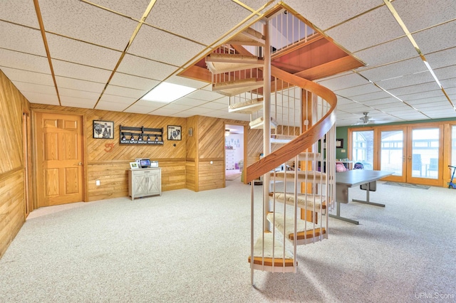 stairway featuring a paneled ceiling, ceiling fan, wood walls, and carpet