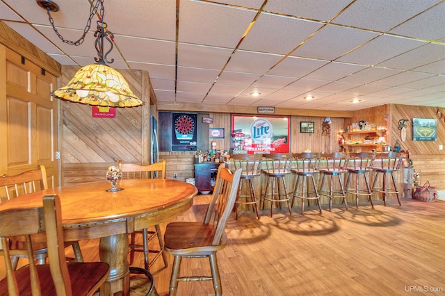 dining space featuring wooden walls, a drop ceiling, and hardwood / wood-style flooring