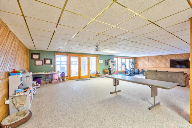 playroom featuring french doors, a drop ceiling, wooden walls, and ceiling fan