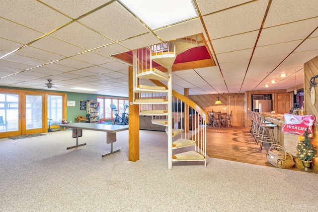 playroom featuring a drop ceiling, wood walls, wood-type flooring, and ceiling fan