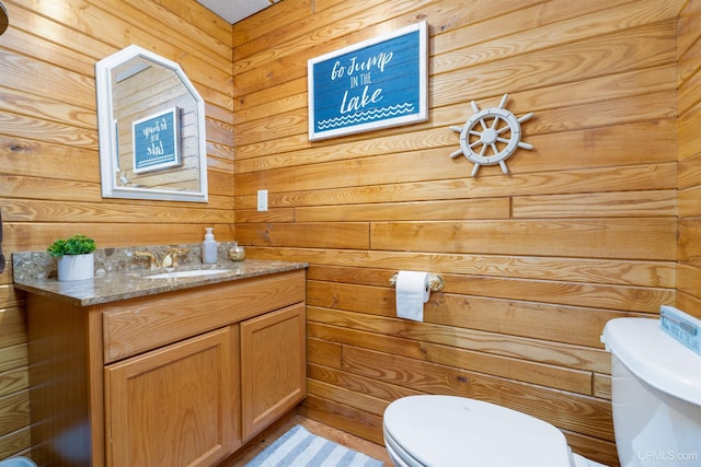 bathroom featuring vanity, wood walls, and toilet