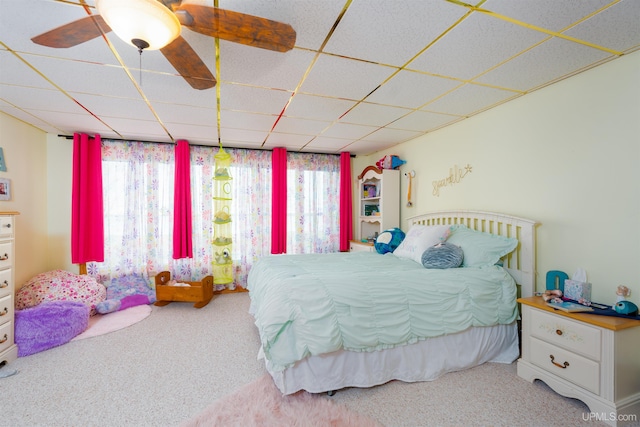 bedroom featuring carpet, ceiling fan, a drop ceiling, and multiple windows