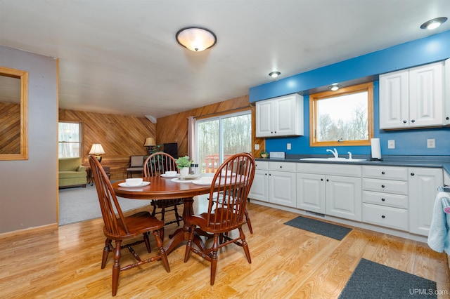 dining space featuring a healthy amount of sunlight, light hardwood / wood-style floors, and wooden walls