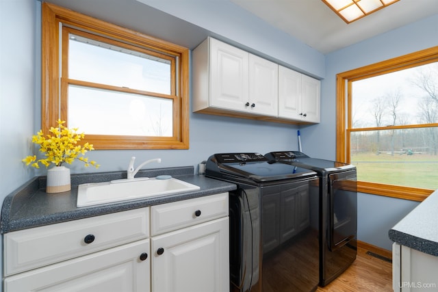 clothes washing area featuring washing machine and clothes dryer, sink, cabinets, and light hardwood / wood-style floors