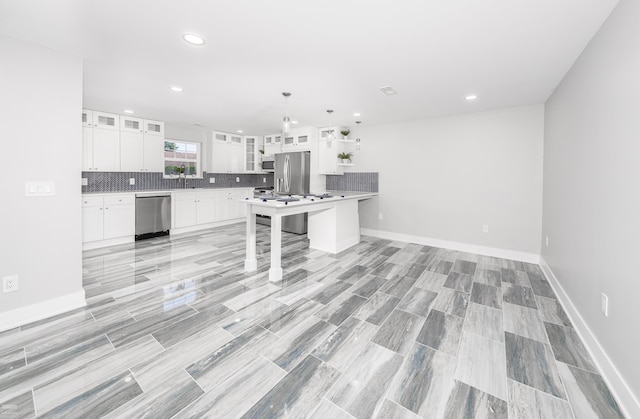 kitchen featuring a kitchen bar, appliances with stainless steel finishes, white cabinets, a kitchen island, and hanging light fixtures