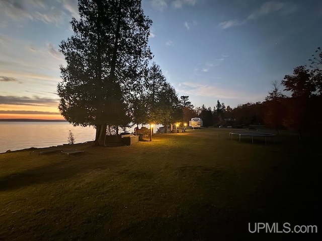 yard at dusk featuring a trampoline and a water view