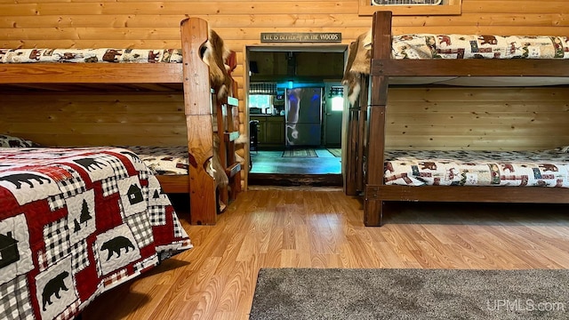 bedroom featuring hardwood / wood-style floors, stainless steel fridge, and wooden walls