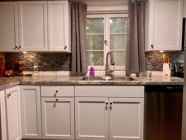 kitchen featuring light stone countertops, white cabinetry, sink, stainless steel dishwasher, and backsplash