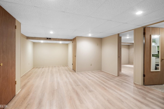 basement with light hardwood / wood-style flooring, a drop ceiling, and wooden walls