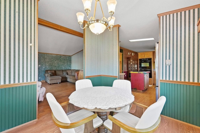 dining room featuring a chandelier, crown molding, light hardwood / wood-style floors, and lofted ceiling