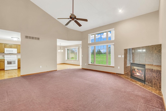 unfurnished living room featuring ceiling fan with notable chandelier, a tile fireplace, light carpet, and high vaulted ceiling