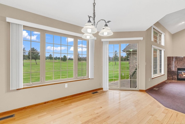 unfurnished dining area with a premium fireplace, a chandelier, a healthy amount of sunlight, and light wood-type flooring