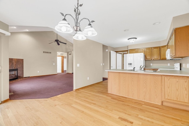 kitchen featuring kitchen peninsula, light wood-type flooring, white appliances, vaulted ceiling, and a tiled fireplace