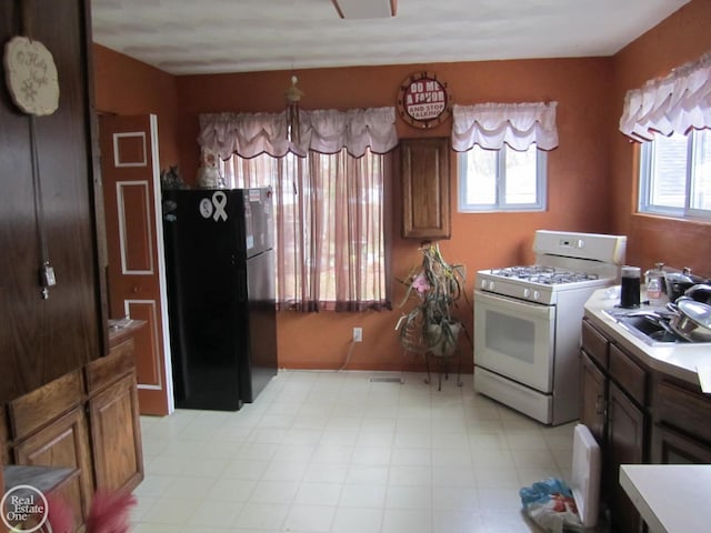 kitchen featuring a wealth of natural light, black fridge, white gas range, and sink