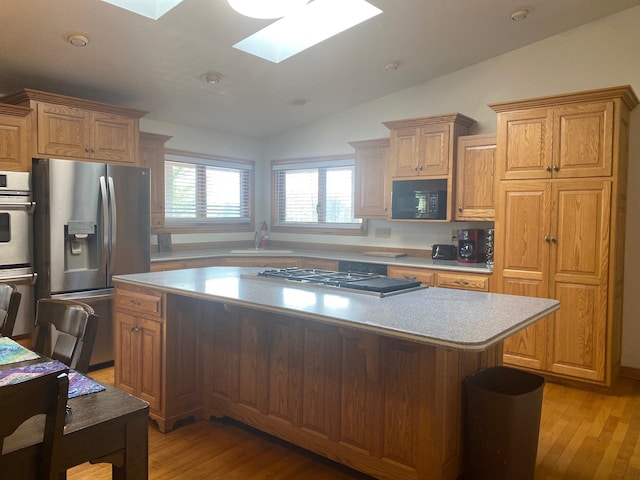 kitchen featuring a center island, lofted ceiling with skylight, sink, light wood-type flooring, and stainless steel appliances