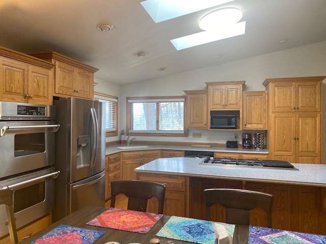 kitchen featuring lofted ceiling with skylight, sink, appliances with stainless steel finishes, and a breakfast bar area