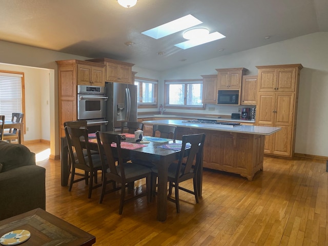 kitchen with appliances with stainless steel finishes, light hardwood / wood-style flooring, lofted ceiling with skylight, and a kitchen island