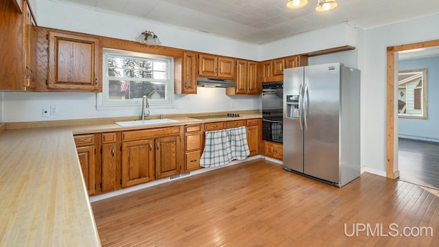 kitchen with electric cooktop, sink, stainless steel fridge, double oven, and light hardwood / wood-style floors