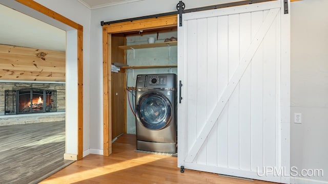 clothes washing area featuring washer / dryer, a barn door, a stone fireplace, and hardwood / wood-style floors