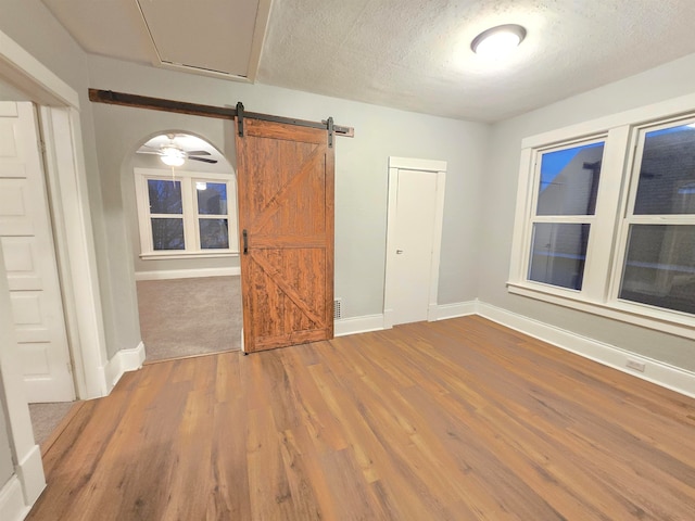 spare room with a barn door, ceiling fan, wood-type flooring, and a textured ceiling