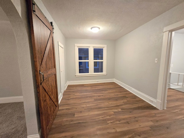 hallway featuring a barn door, dark wood-type flooring, and a textured ceiling