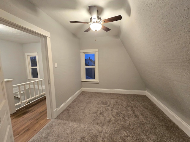 bonus room featuring a textured ceiling, ceiling fan, dark carpet, and lofted ceiling