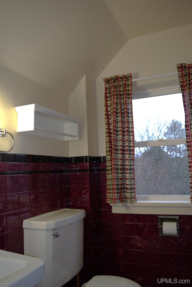 bathroom featuring vaulted ceiling, toilet, and tile walls